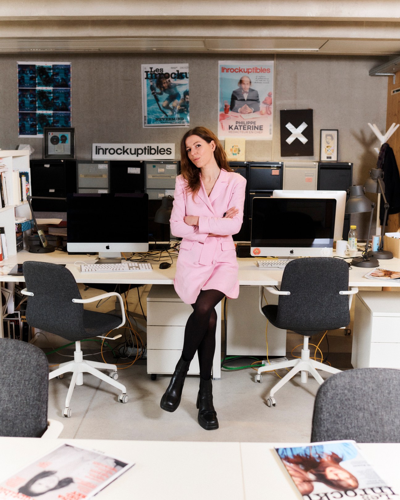 Carole Boinet sitting at desk in Les Inrockuptibles magazine office with posters on wall behind her