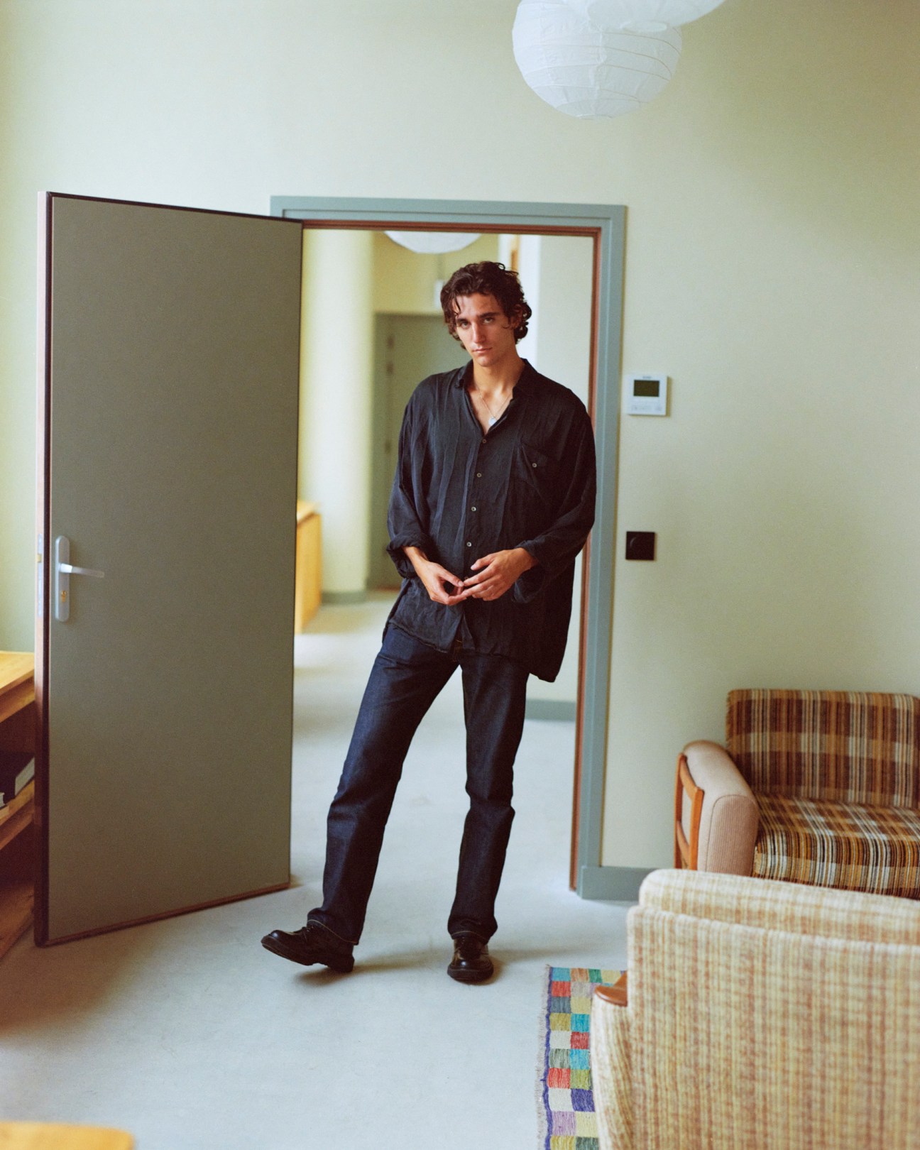Tamino standing in a doorway wearing a dark button-up shirt and jeans in an interior setting