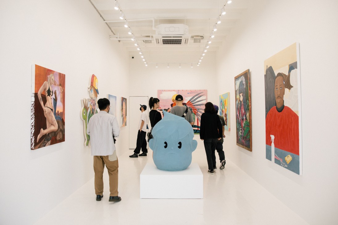 Gallery visitors viewing colorful contemporary paintings on white walls with a blue sculptural object on white pedestal
