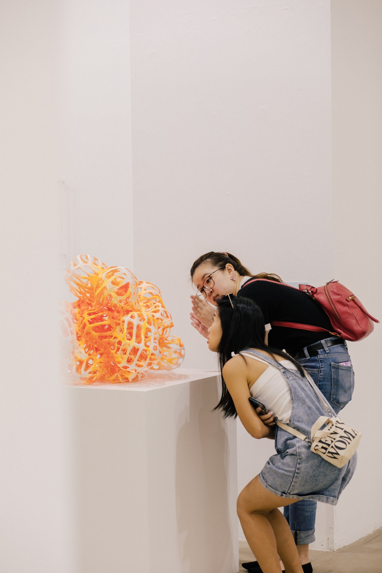 Two women viewing Jason Lim's orange sculptural artwork displayed on white pedestal at SEA Focus art fair