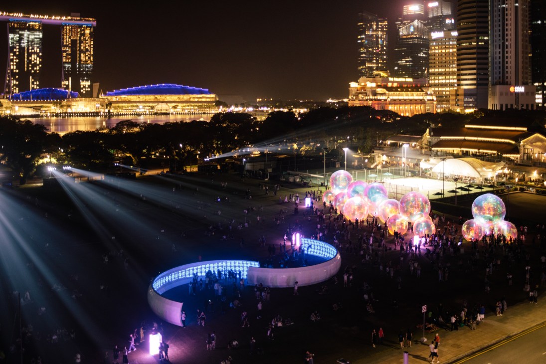 Nighttime outdoor art installation with illuminated spherical bubbles and curved structure surrounded by crowds in Singapore