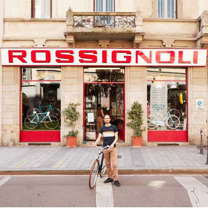 Matia Bonato standing with his bicycle outside the red-fronted Rossignoli bike shop storefront in Milan