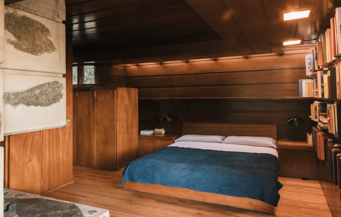 Built-in bed with blue coverlet surrounded by wooden cabinetry and shelving in a modernist bedroom.