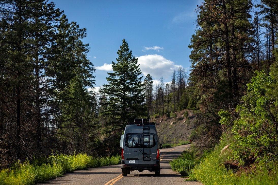 Gray camper van driving on a winding road through forested hills in Durango, Colorado