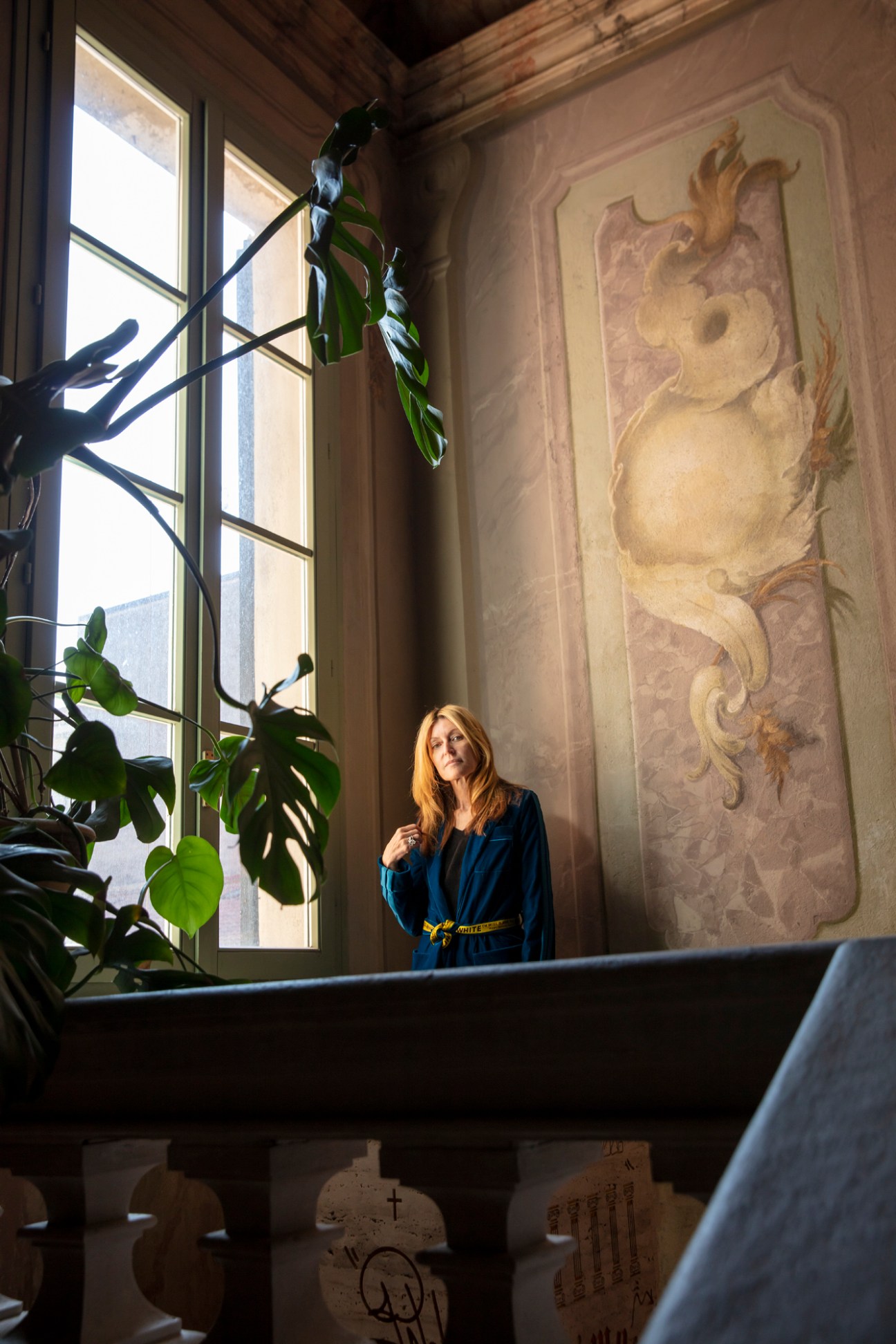 Umberta Gnutti Beretta in an elegant interior with ornate wall relief and large windows with plants