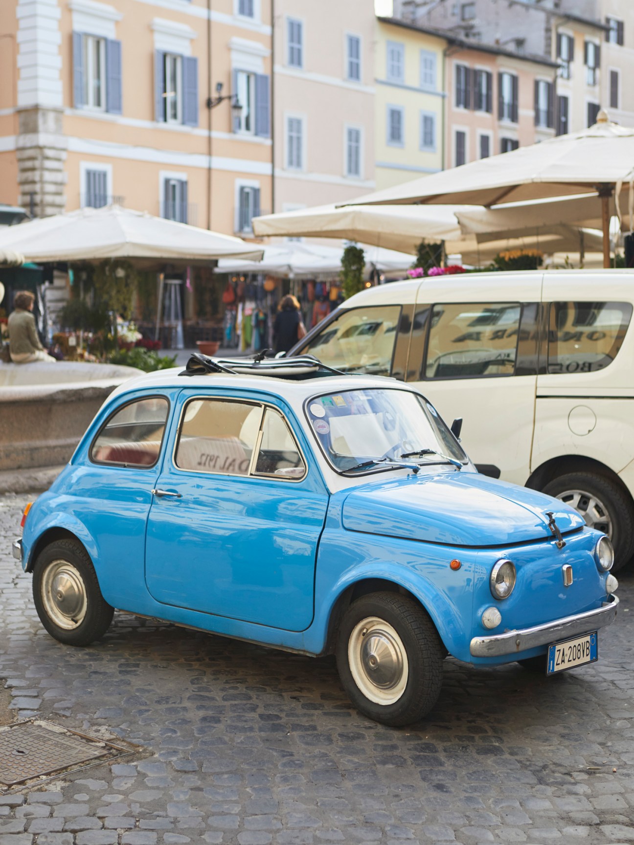 A blue vintage Fiat 500 parked on cobblestone street in Italian town square
