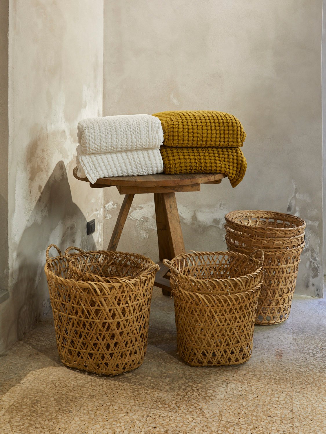 Folded towels and woven baskets displayed on wooden stool against weathered wall
