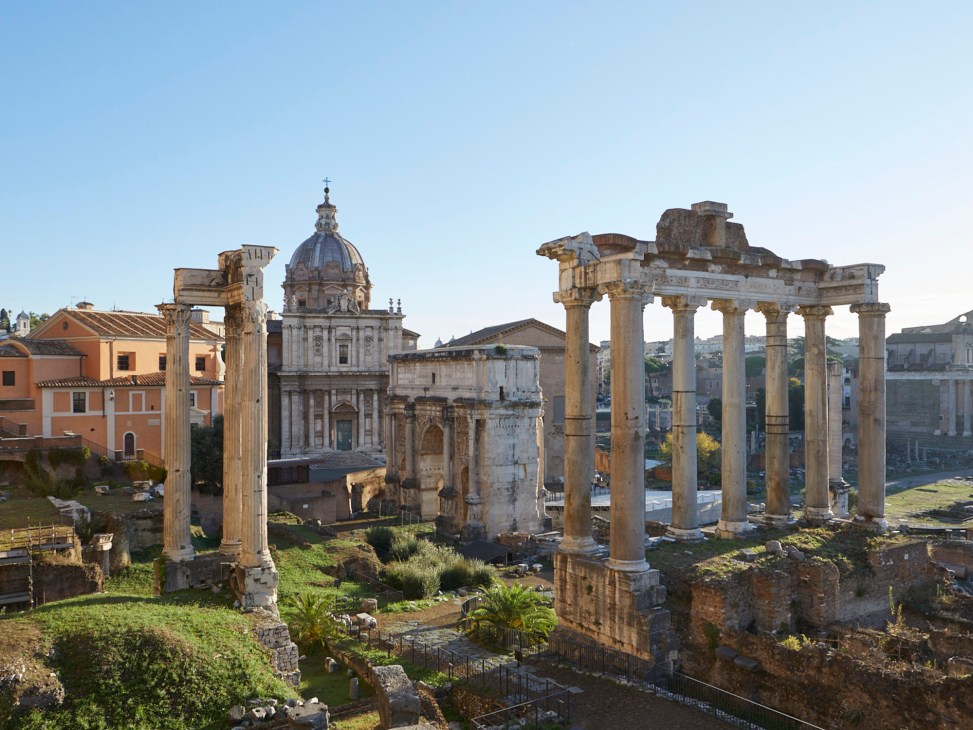 Ancient Roman ruins of The Forum with columns, arches and stone structures under blue sky