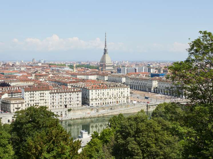 Panoramic view of Turin with the Mole Antonelliana tower dominating the skyline and the Po River flowing through the city below.