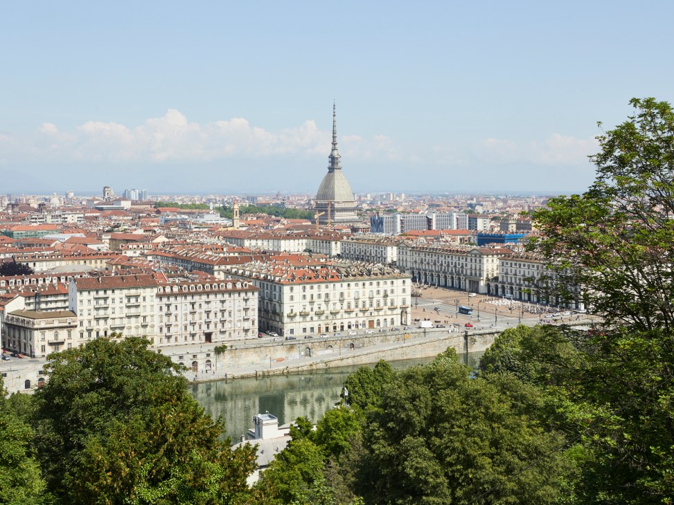 Panoramic view of Turin with the Mole Antonelliana tower dominating the skyline and the Po River flowing through the city below.