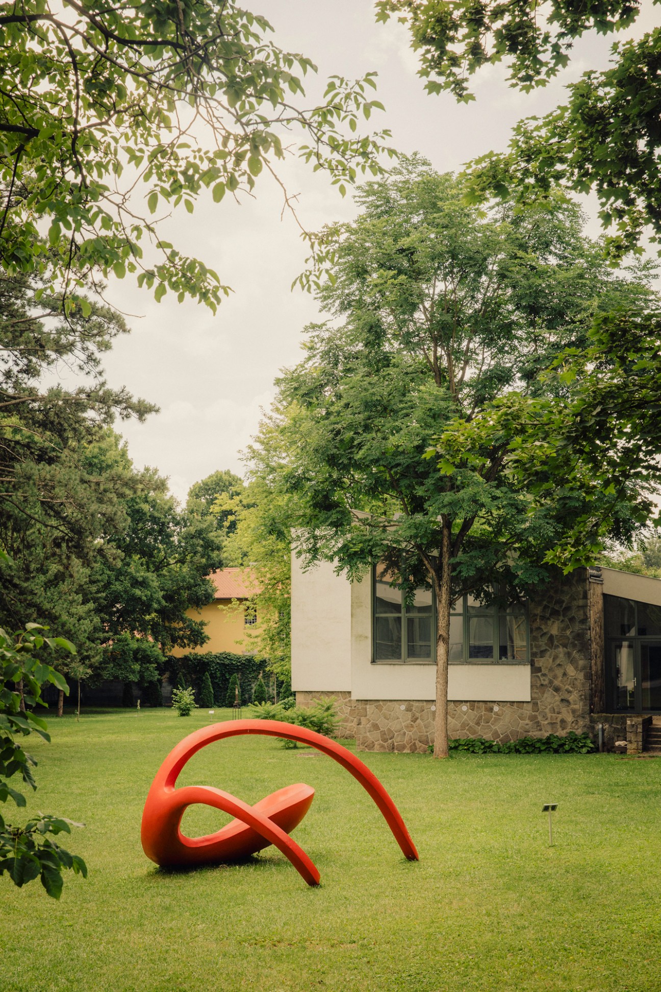 Orange sculptural artwork on green lawn with modernist house and trees in background