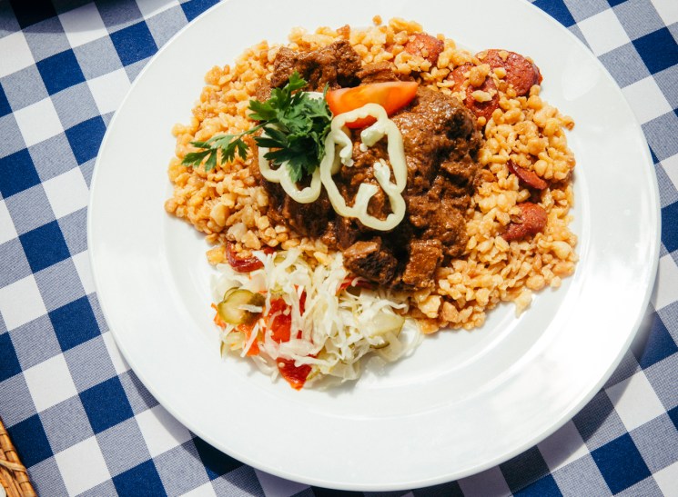 Traditional Hungarian meal with rice, meat stew, and salad served on white plate with checkered tablecloth