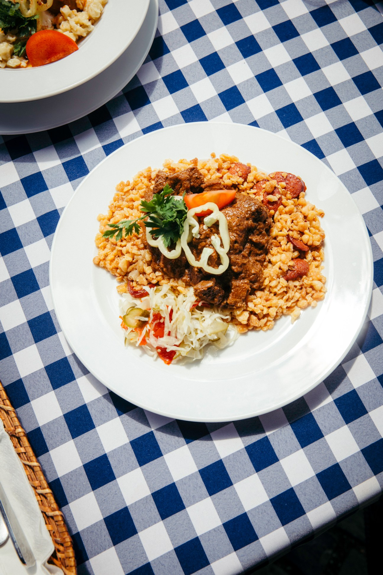Traditional Hungarian meal with rice, meat stew, and salad served on white plate with checkered tablecloth