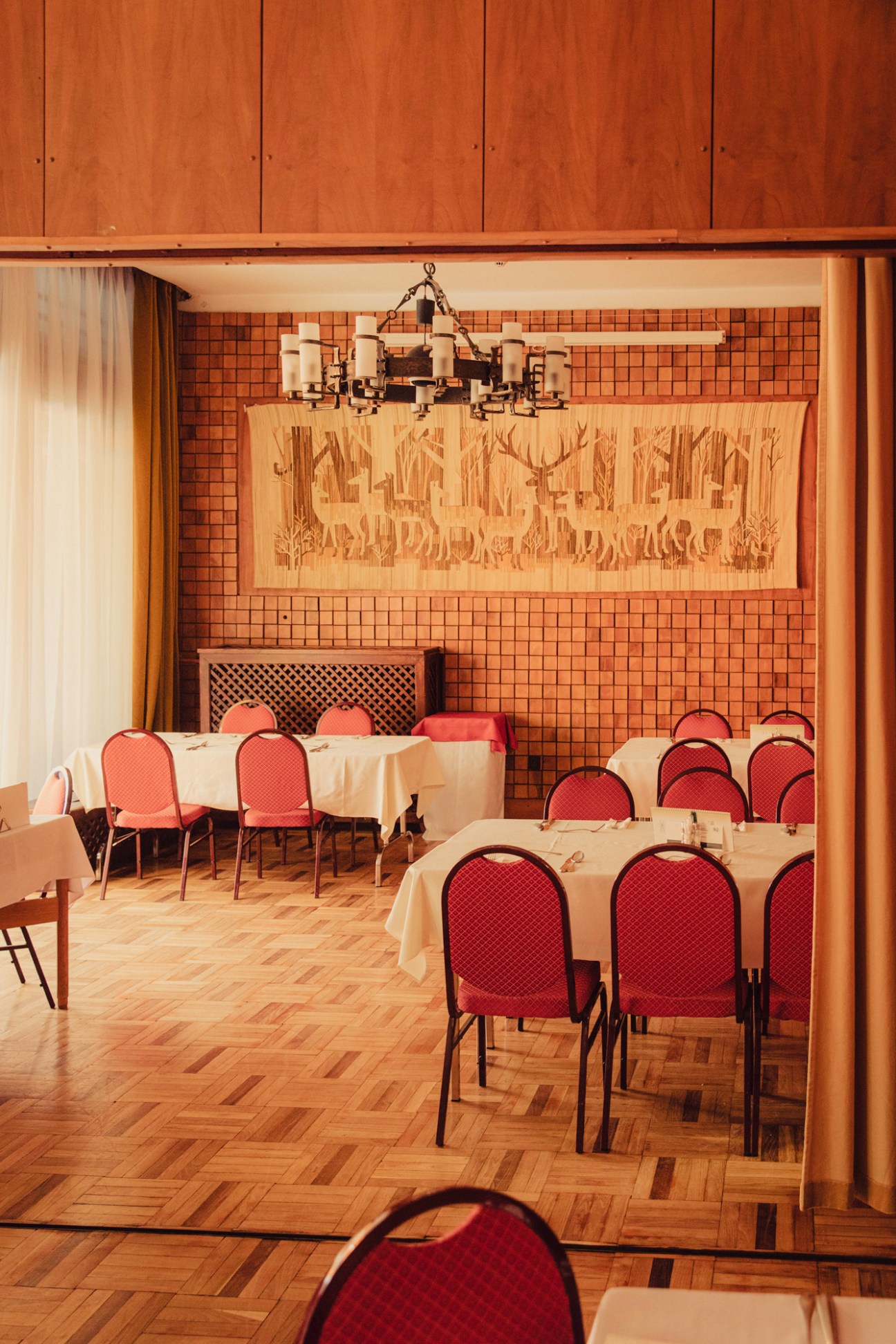 Traditional Hungarian restaurant interior with wood paneling, orange upholstered chairs, and white tablecloths