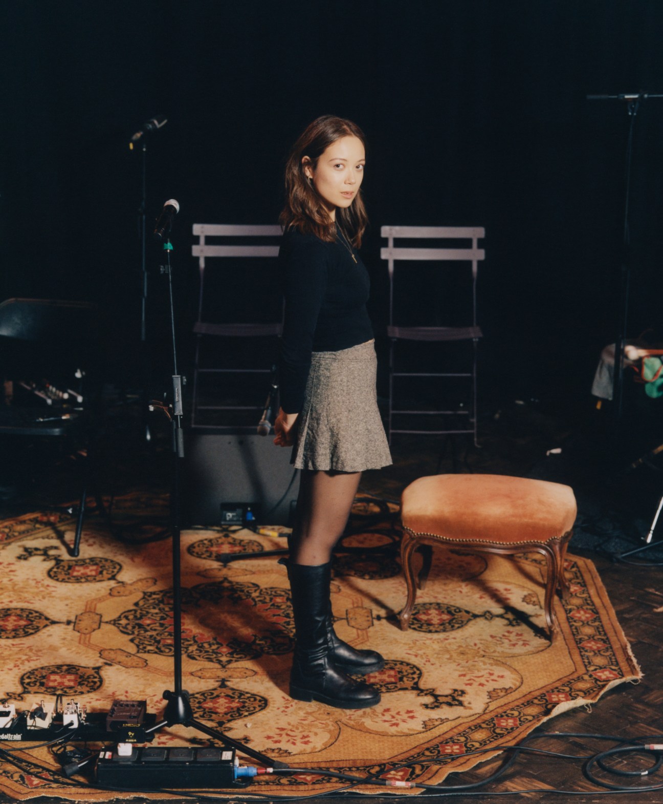 Laufey performing in a recording studio setting, wearing black clothing and standing near a microphone
