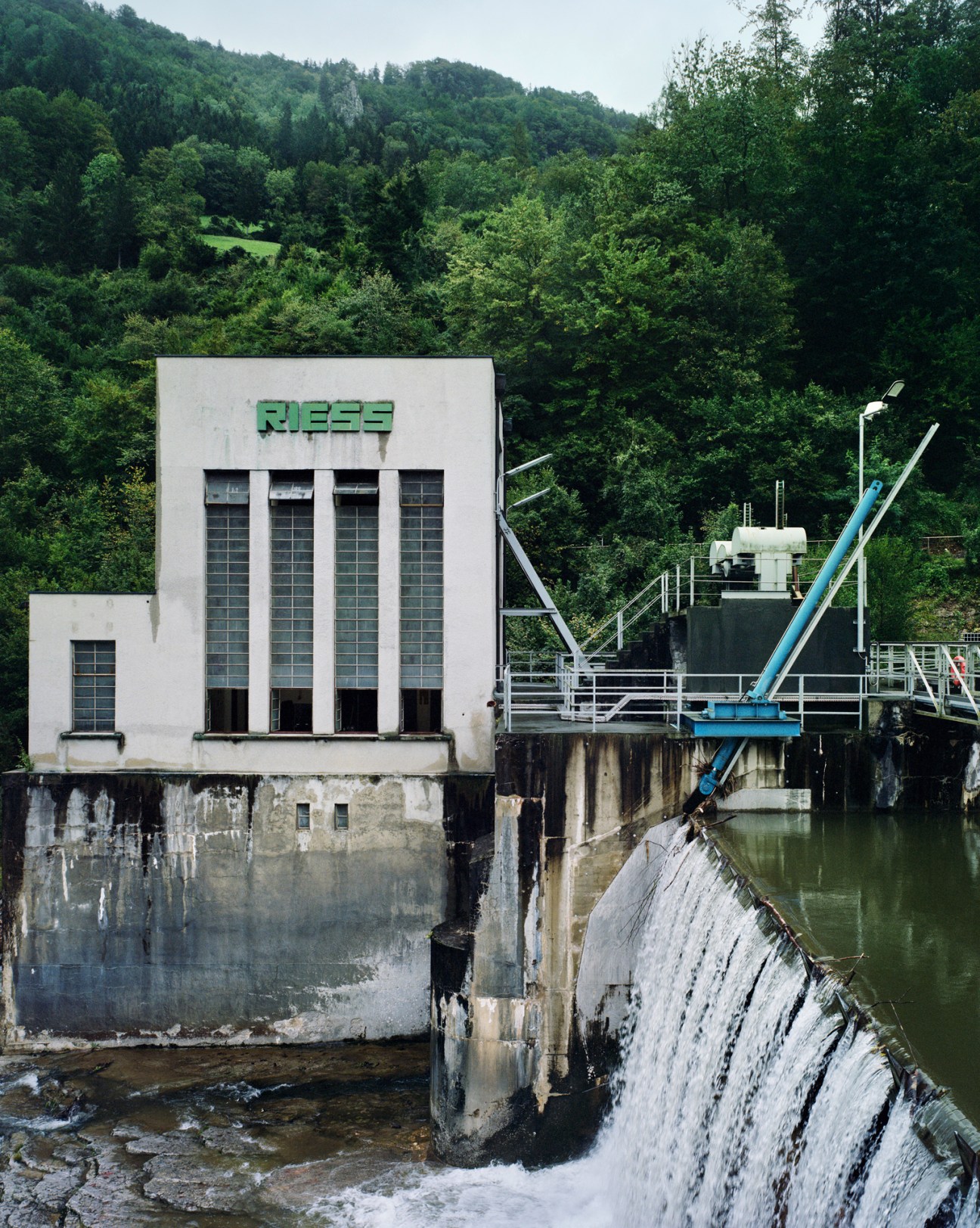 Riess hydroelectric power plant building with green Riess signage beside flowing water in Austrian Alps valley
