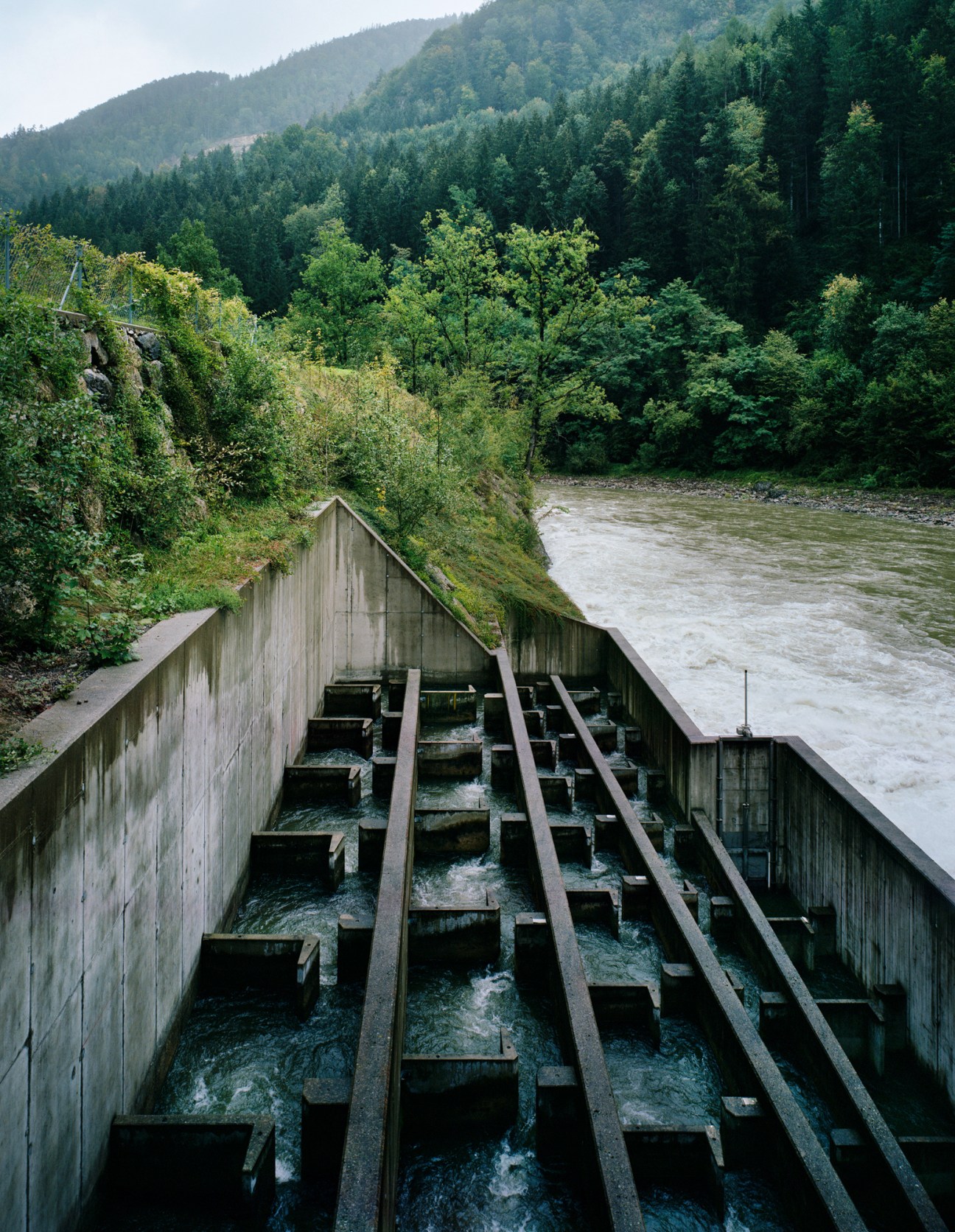 Hydroelectric power plant intake on the Ybbs river in Austria with forested mountains in background.