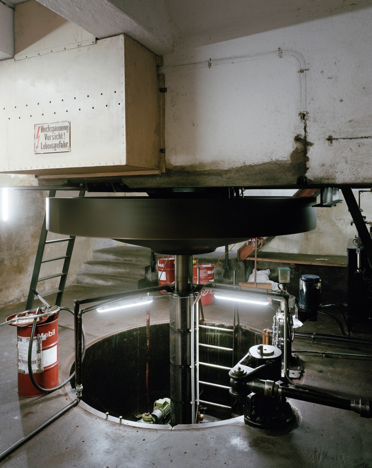 Industrial hydroelectric power plant machinery with large turbine and control equipment in factory basement.