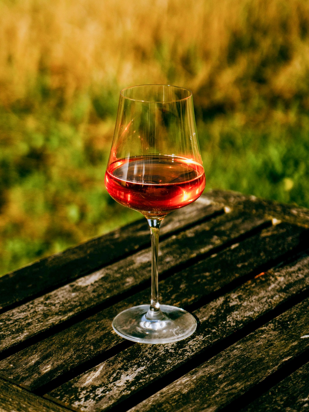 Glass of Offbeat Wine's Skinny Dip sparkling wine on wooden surface with blurred vineyard background