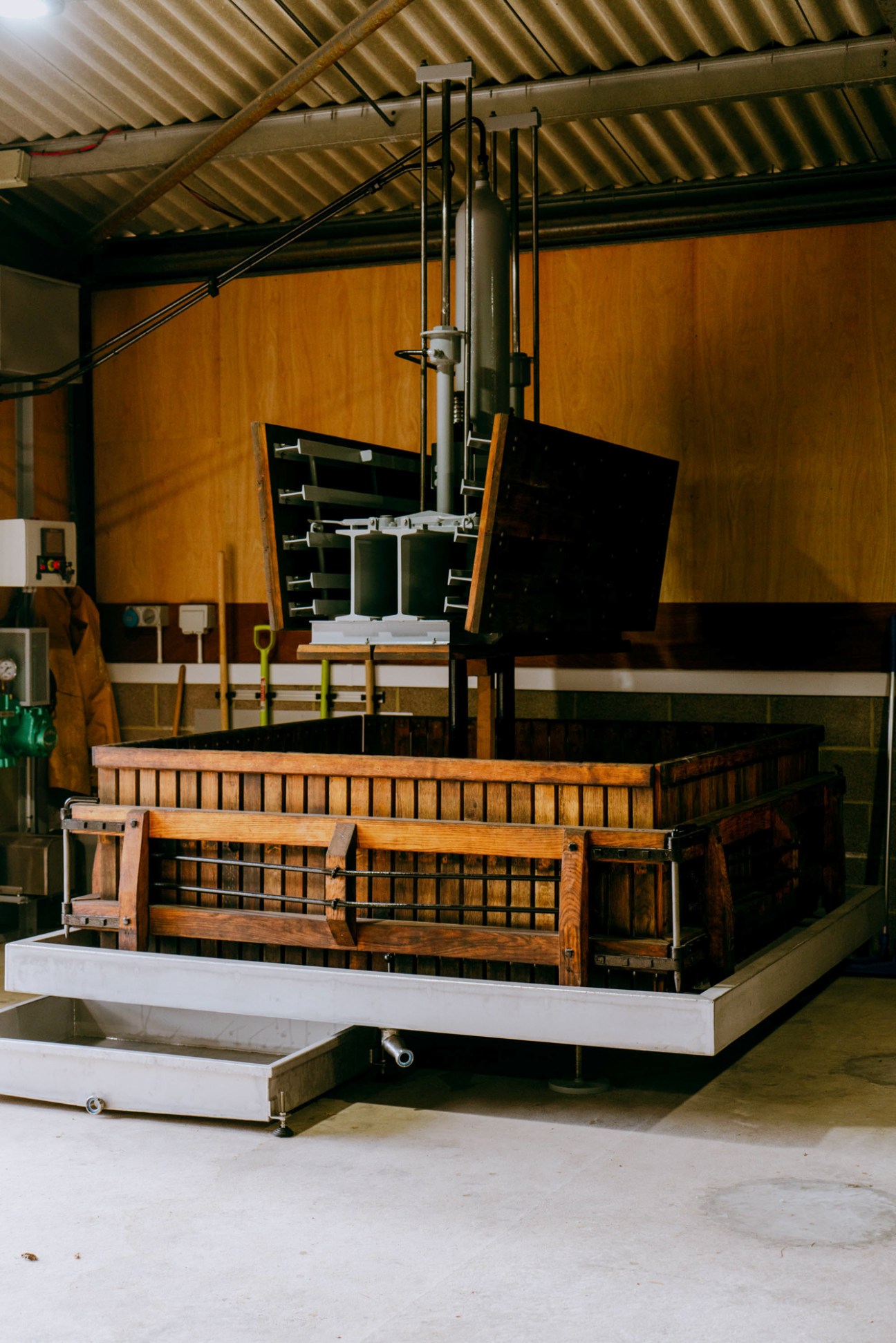 Large wooden wine press with metal mechanism in industrial winery setting with exposed ceiling beams