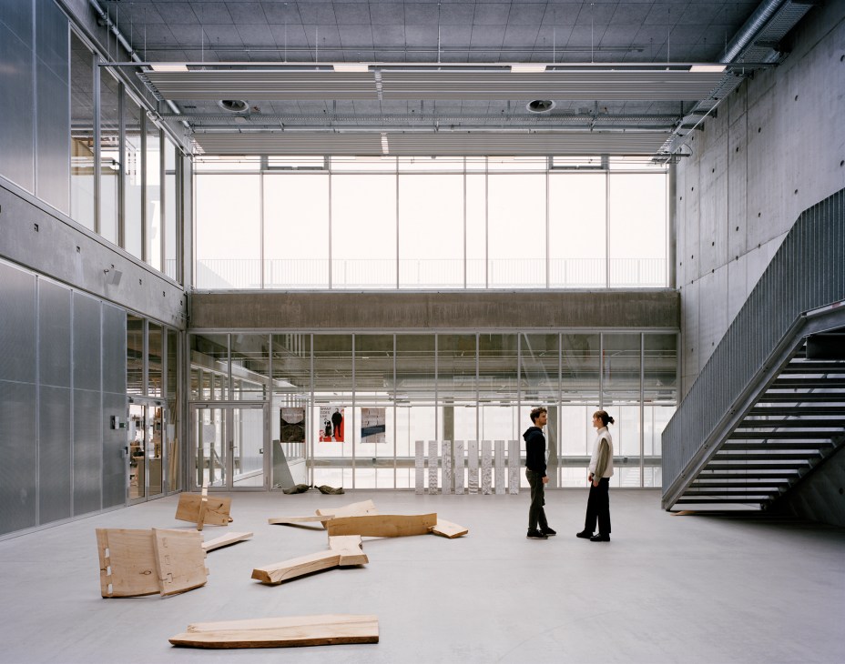 Modern architecture school interior with concrete walls, large windows, wooden sculptural elements on floor, two people talking