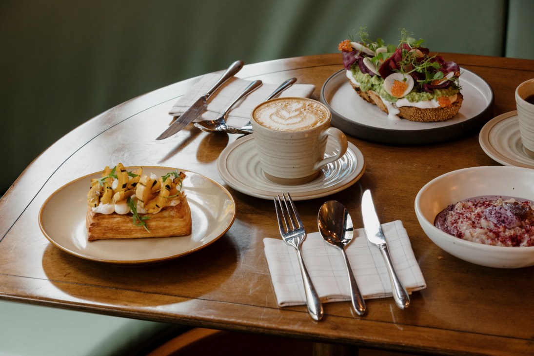 Artfully plated breakfast dishes and latte with foam art on wooden table with white ceramics and silverware