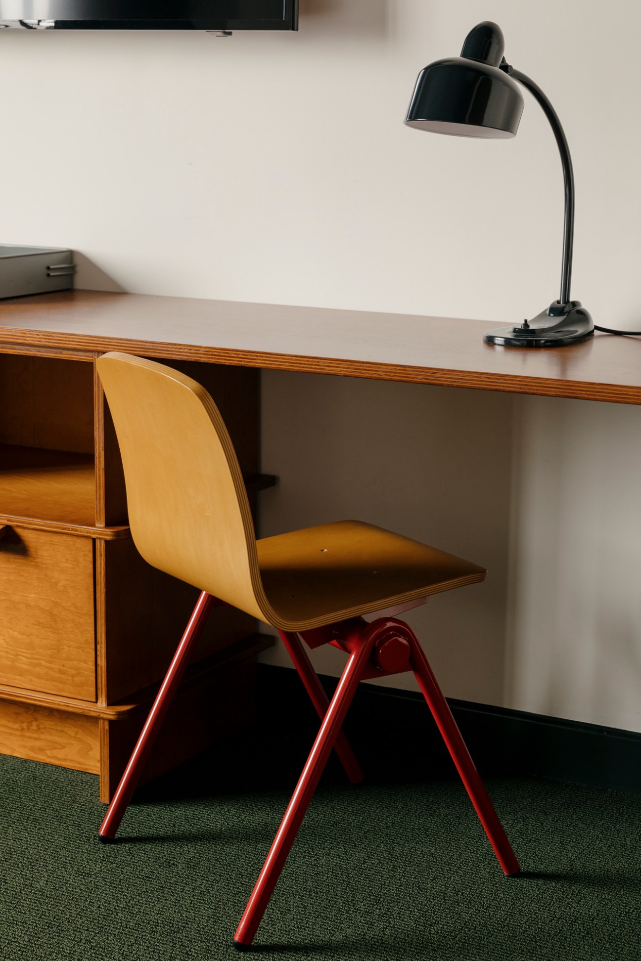 Mid-century modern workspace with wooden desk, yellow chair with red legs, black desk lamp and built-in storage