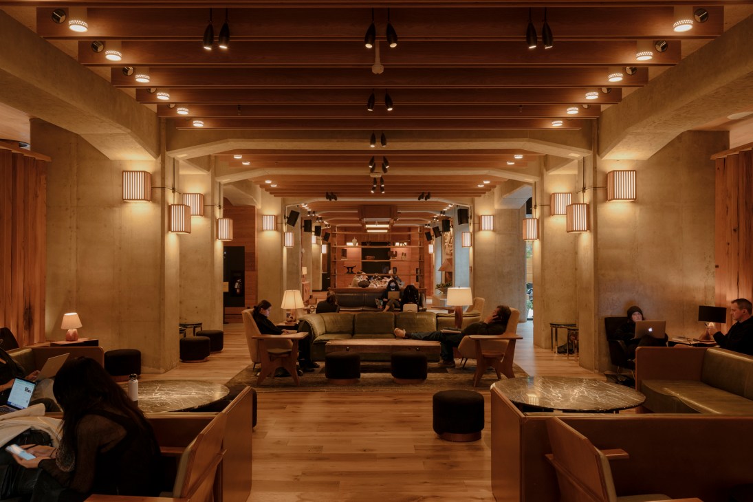 Modern hotel lobby with exposed wooden beams, warm lighting, and guests working in comfortable seating areas