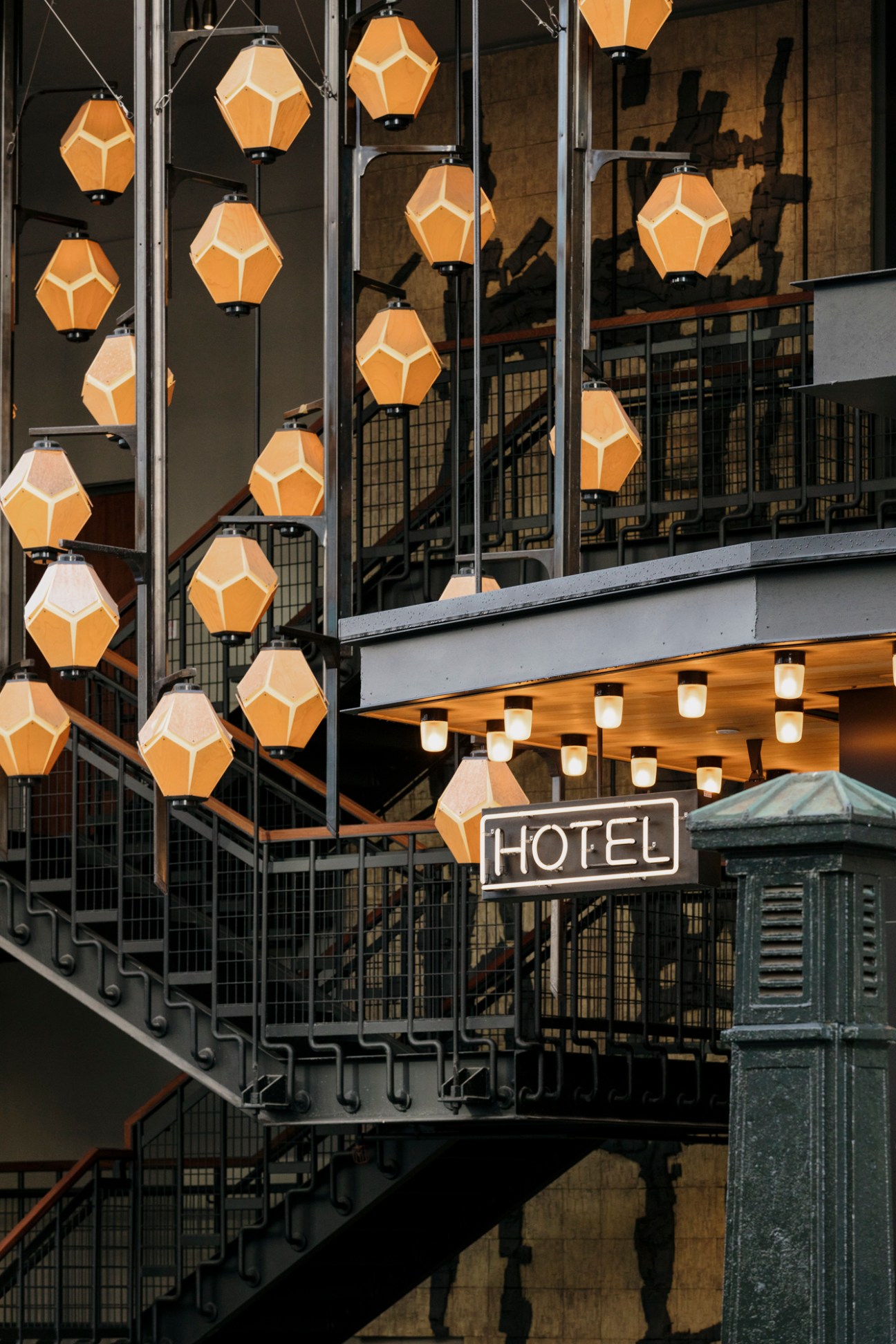Geometric pendant lights hang outside industrial-style hotel building with fire escape stairs and hotel signage