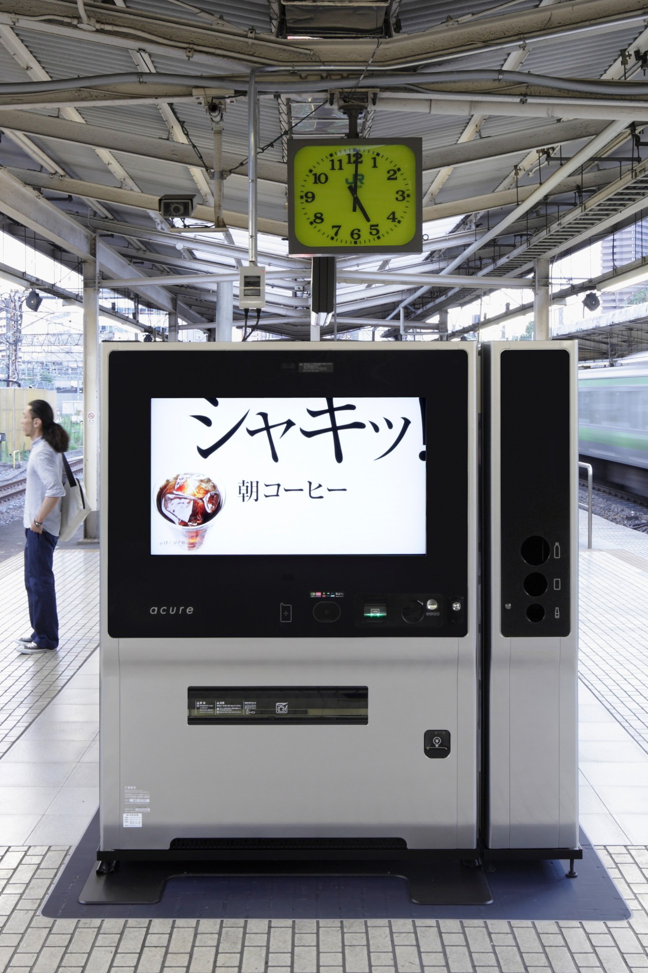 Acure vending machine with green display screen and sleek design at Japanese train station platform