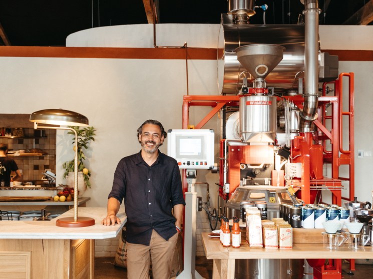 Adam Genovese standing in his coffee roastery with industrial equipment and large orange letter signage