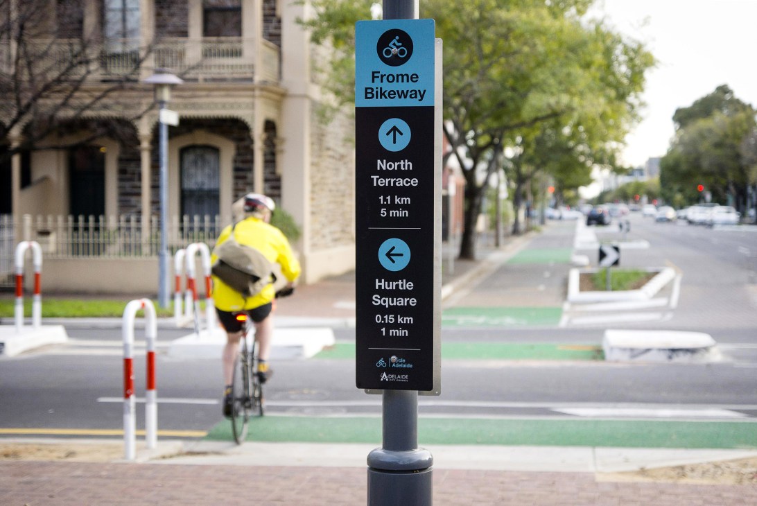 Bright yellow cycling wayfinding sign in Adelaide showing directions and travel times to various city destinations