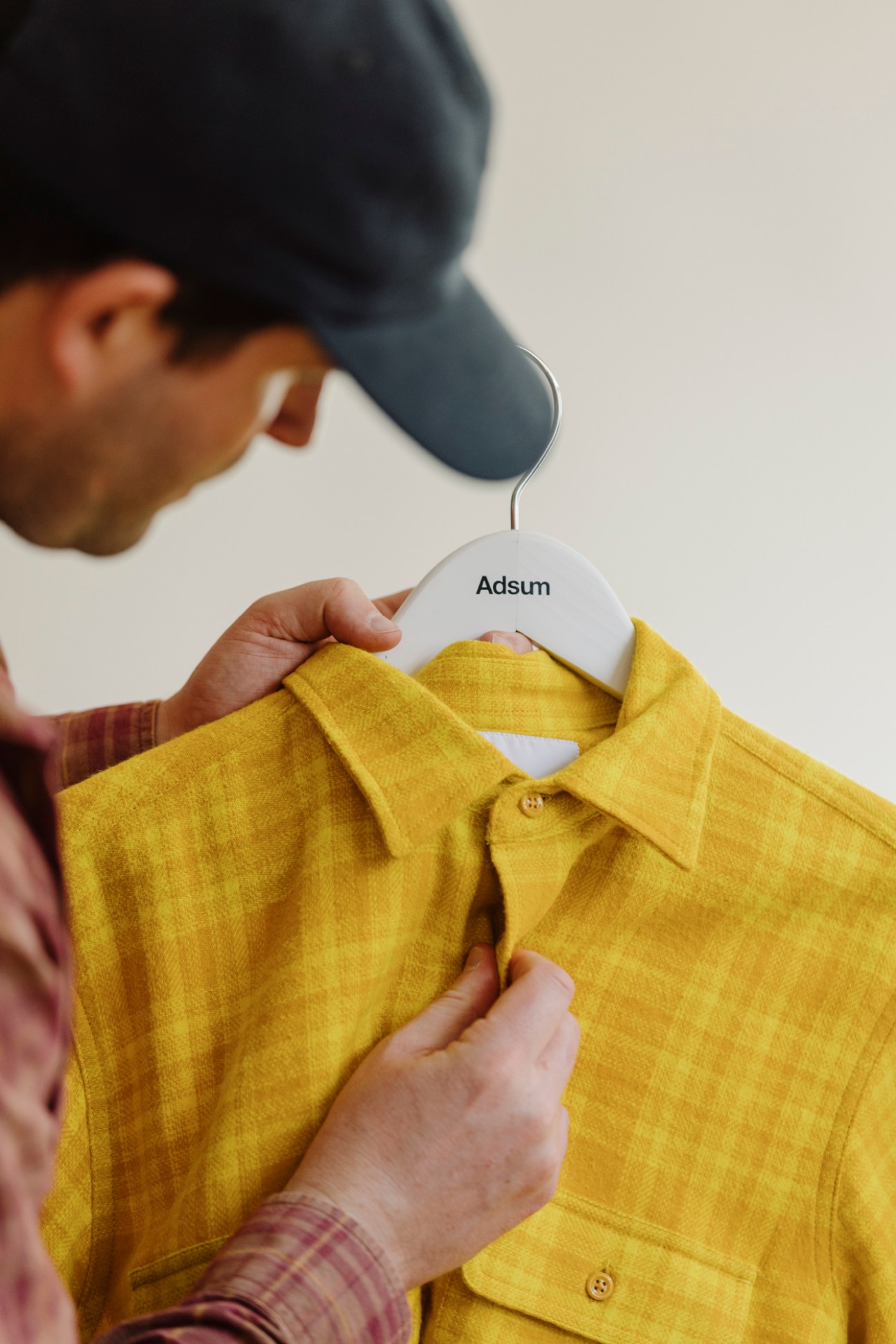 Person examining yellow Adsum shirt on hanger showing detailed construction and quality