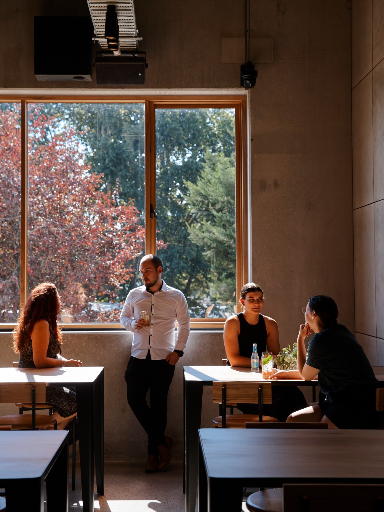 Interior dining space with people seated at tables by large windows overlooking autumn trees
