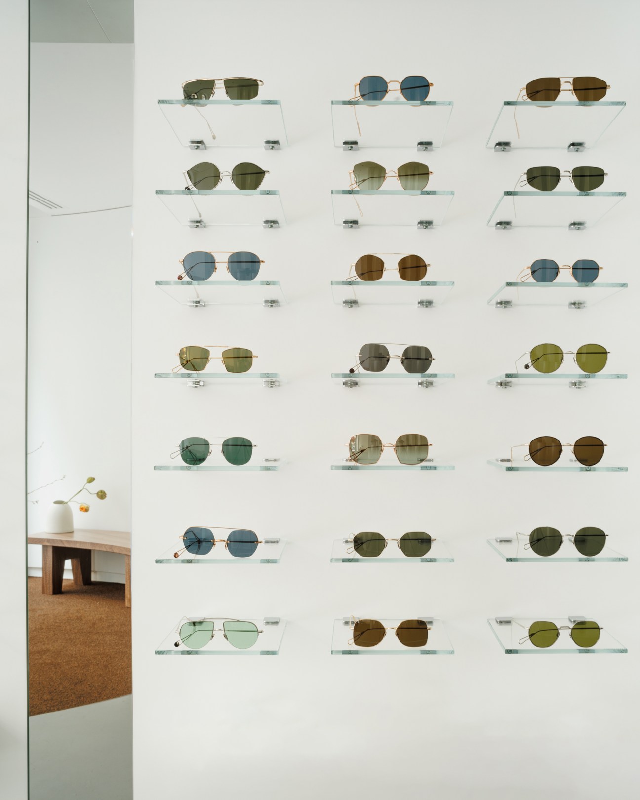 Wall display of various sunglasses mounted on glass shelves in Ahlem's minimalist Paris store