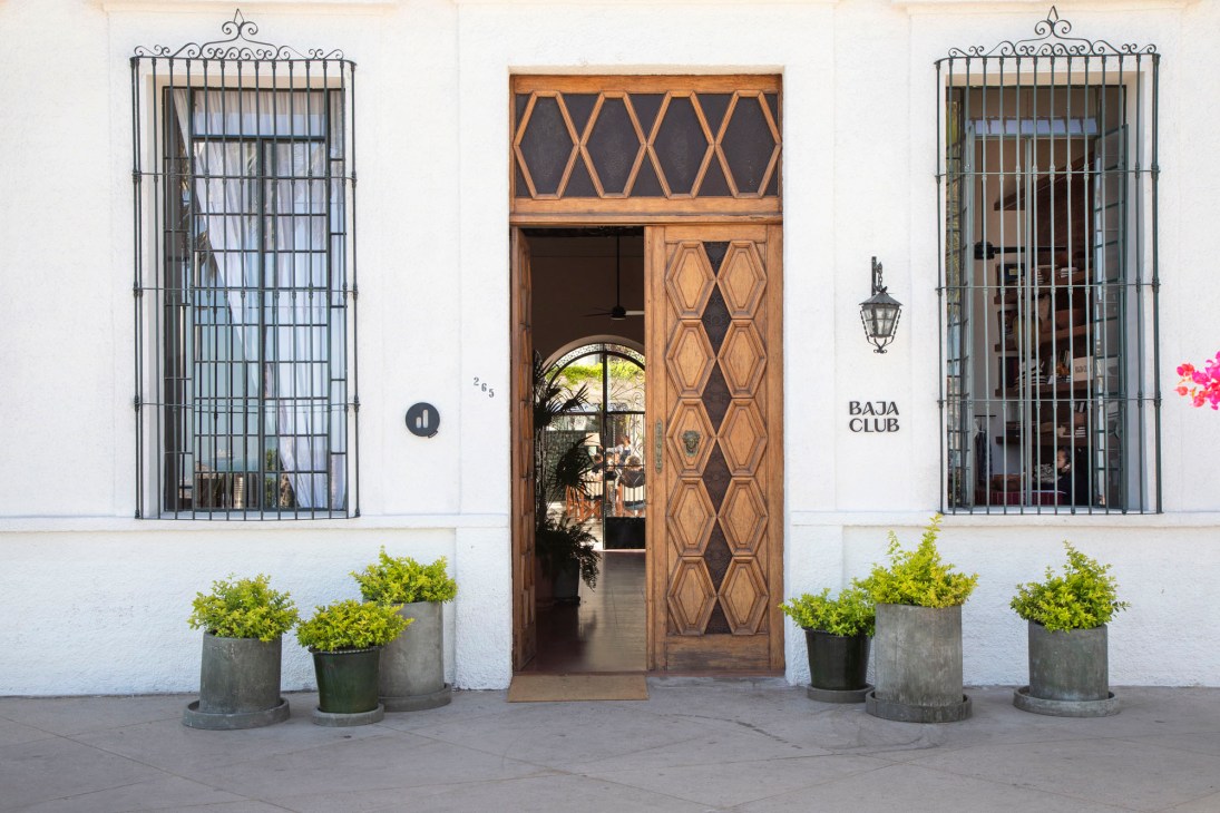 Baja Club's colonial-style entrance with wooden door, ornate cast-iron grills and white stucco facade.