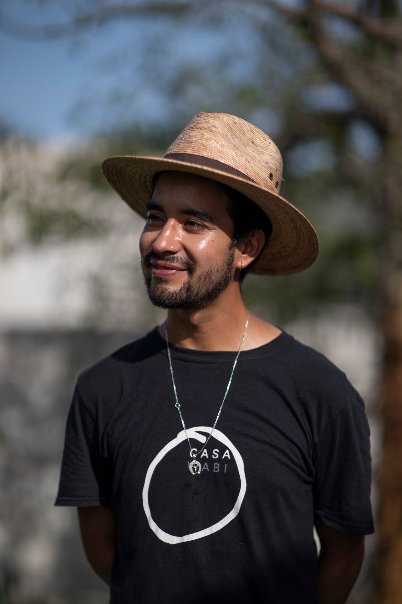 Man in straw hat and black Casa Wabi t-shirt smiling outdoors