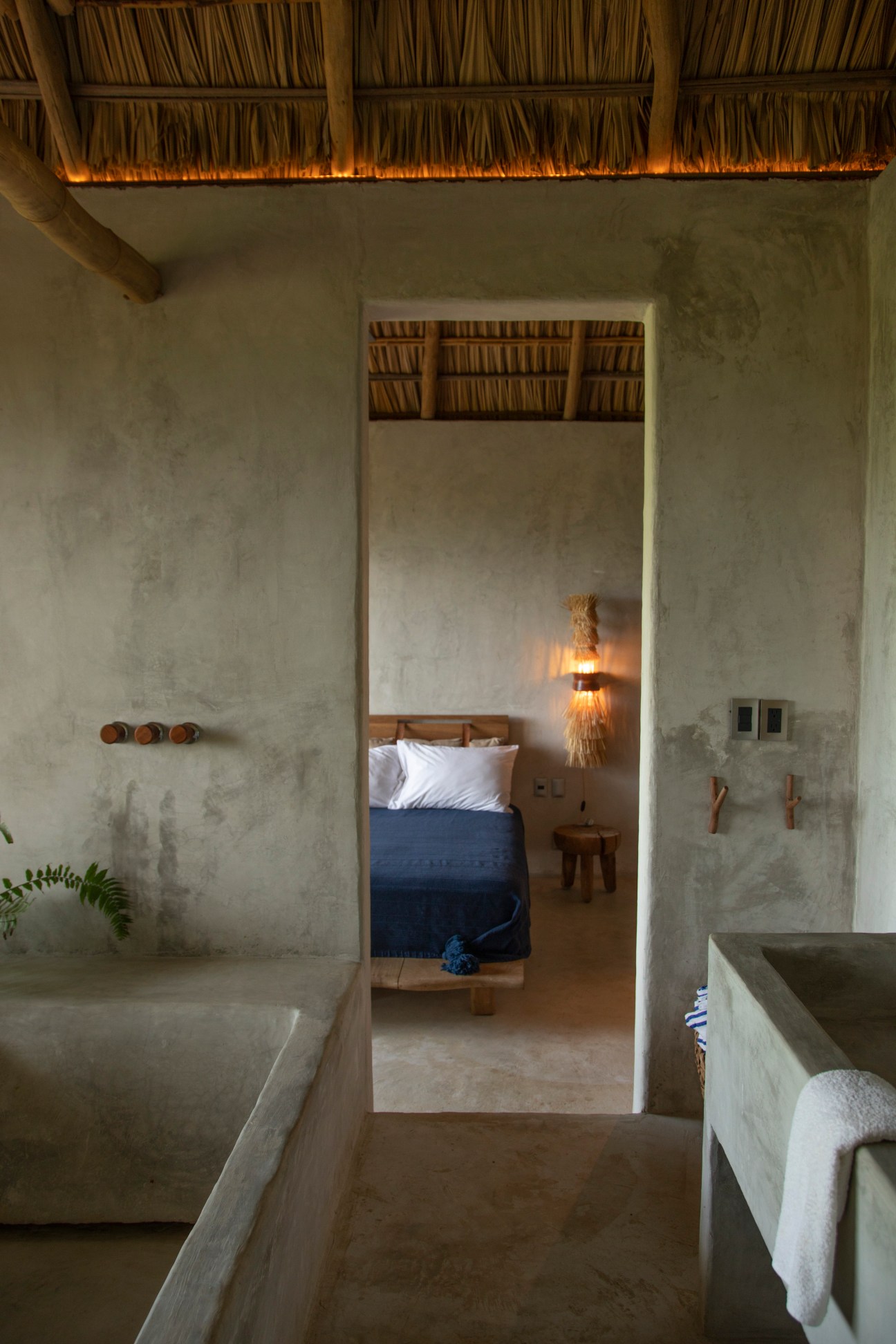 Bathroom view into bedroom with blue bedding and white pillows in concrete hotel room