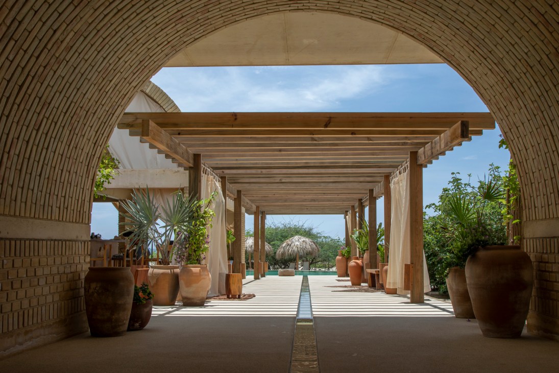 Curved brick archway framing wooden pergola walkway with terracotta pots and tropical plants