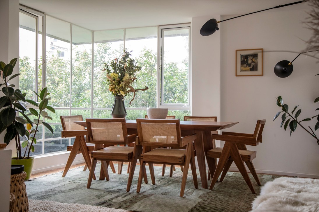 Modern dining room with wooden table, cane-back chairs, large windows, and mid-century lighting