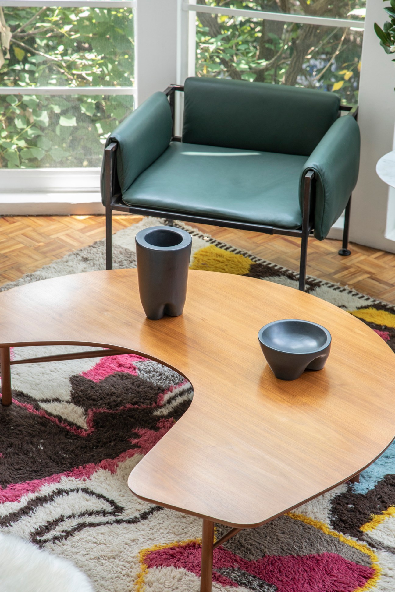 Modern living room with dark green leather chair, round wooden coffee table, and colorful geometric rug