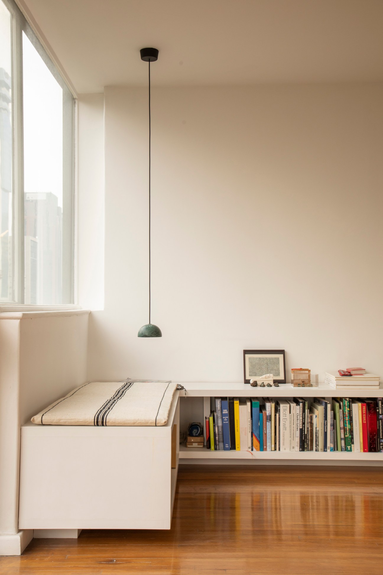 Built-in white bench seating with striped cushion next to bookshelf with colorful books and pendant light