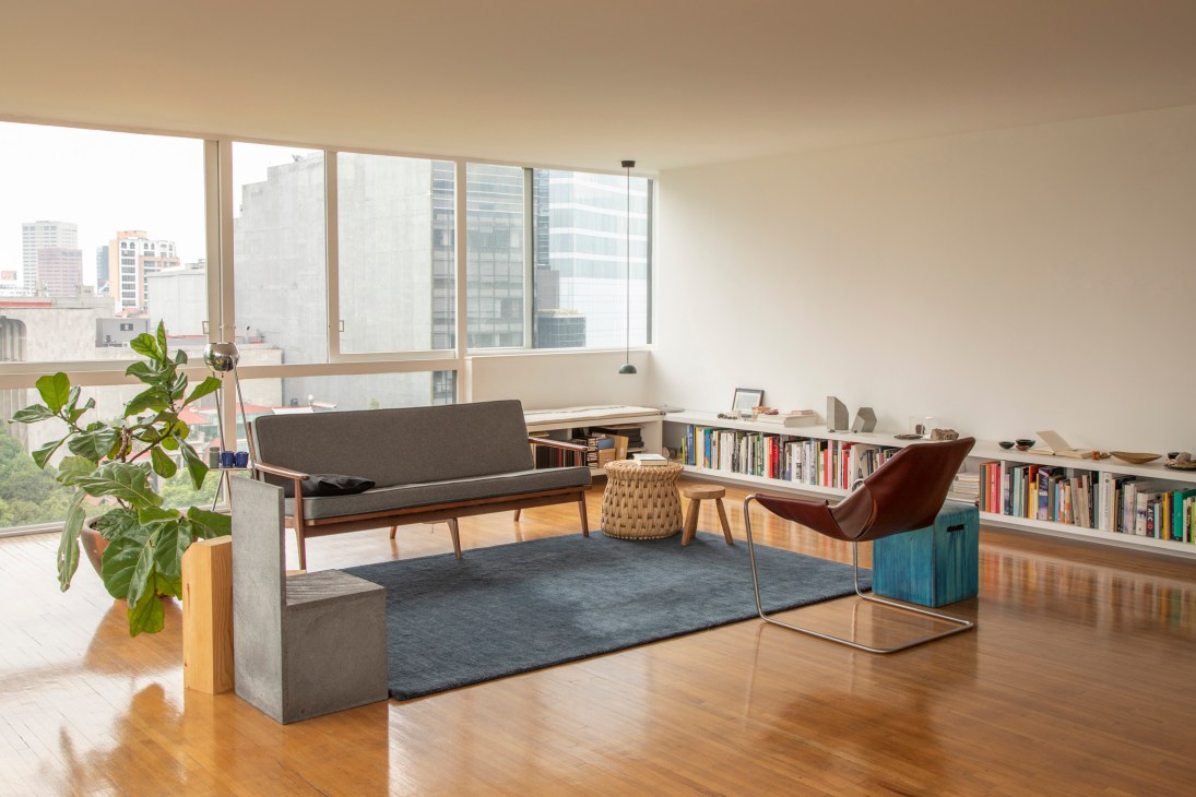 Modern minimalist living room with gray sofa, brown leather chair, blue rug and built-in bookshelves