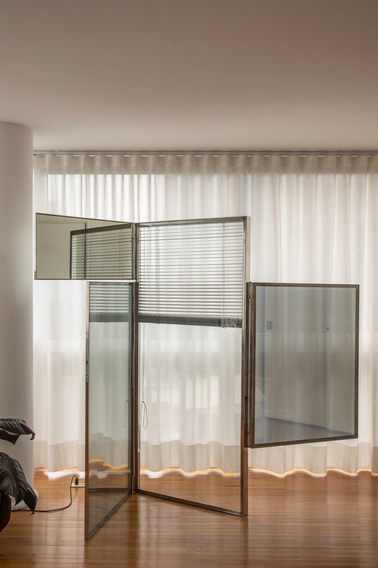 Reflective folding screen panels with geometric frames standing on wooden floor in minimalist bedroom