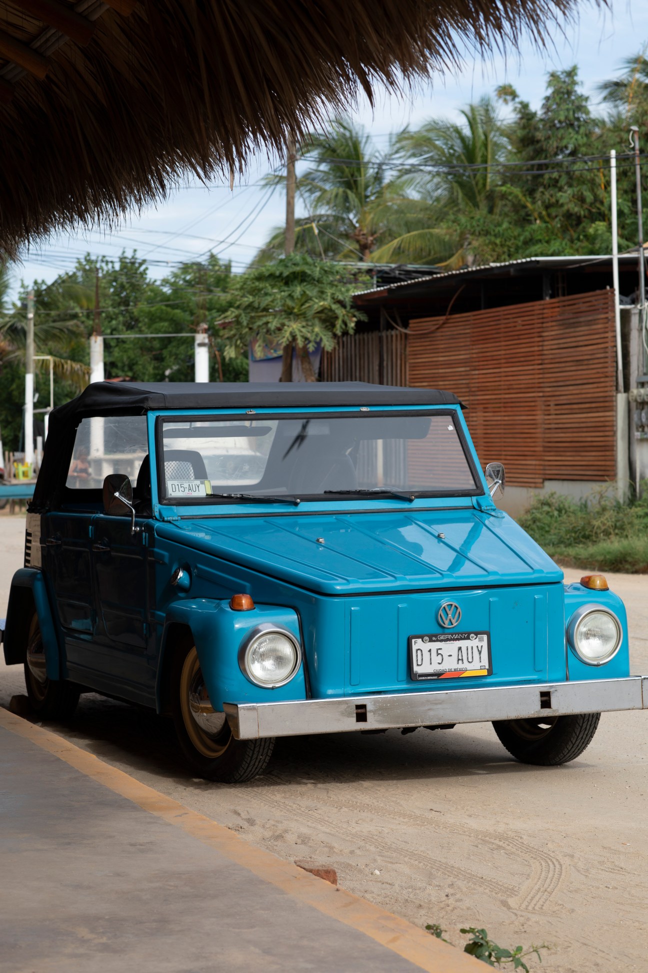 Blue Volkswagen convertible with black soft top parked on paved road in tropical setting