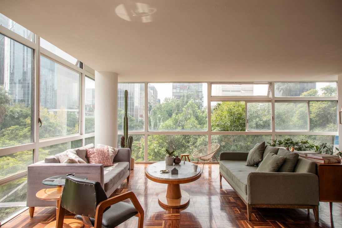 Modern living room with floor-to-ceiling windows, gray sofas, wooden coffee table, and city view