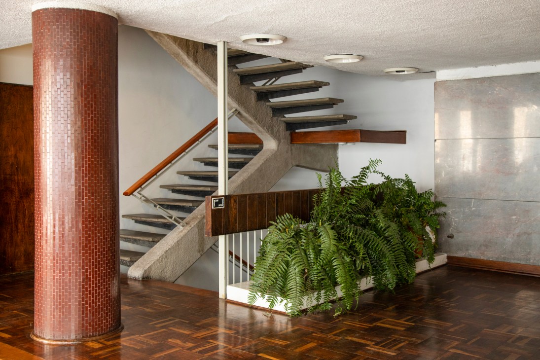 Modern staircase with geometric zigzag design, red mosaic column, and large fern plant in contemporary interior
