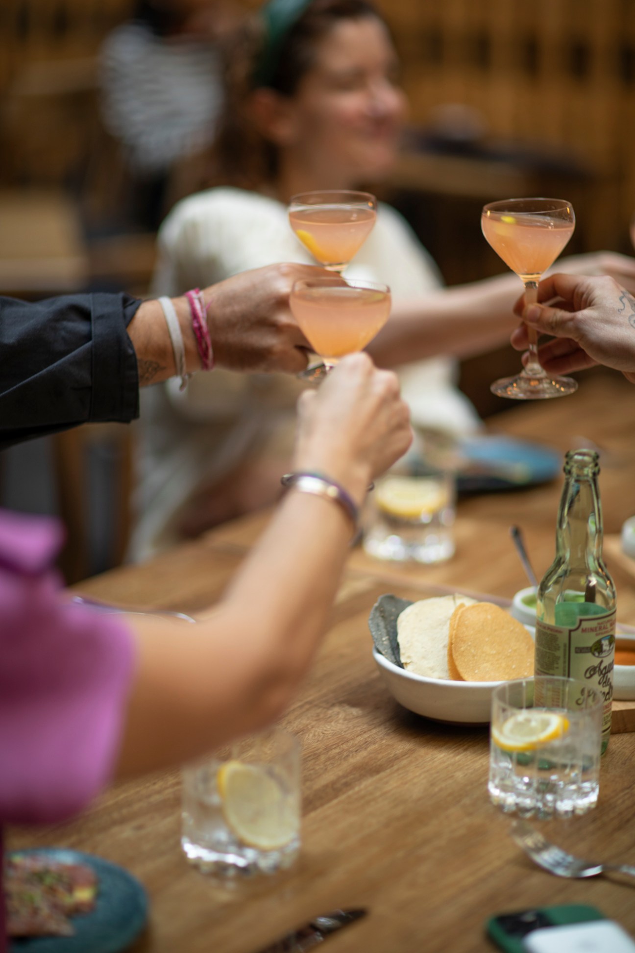 People toasting with cocktails at a wooden table during a dinner discussion.