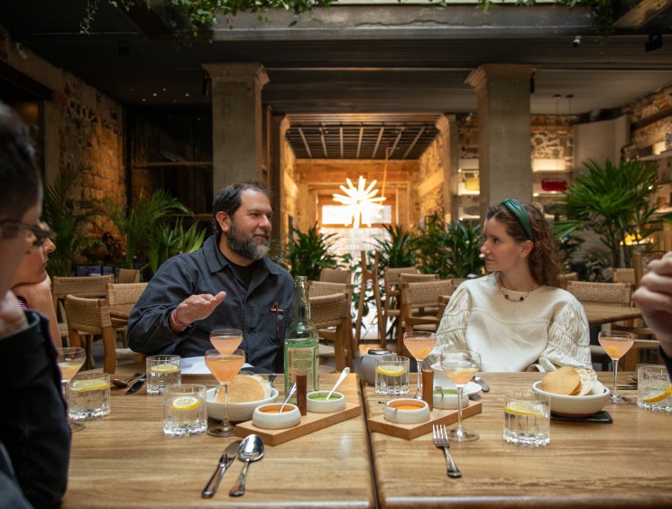 A group of people dining at a rustic restaurant with stone walls, exposed beams, and lush plants