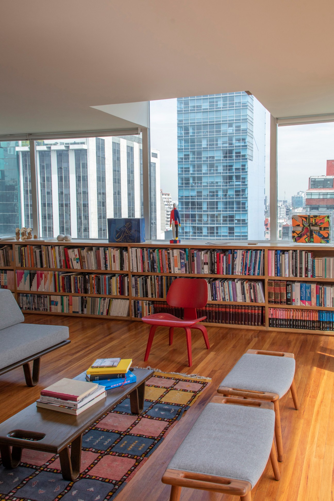 Modern apartment interior with floor-to-ceiling bookshelves, red chair, and city view through large windows